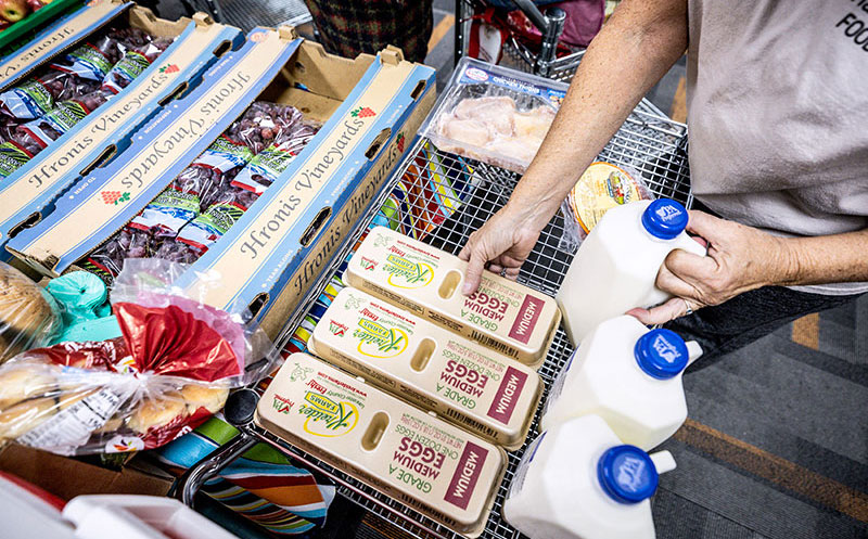Person placing groceries including eggs and milk into a cart at a food distribution site